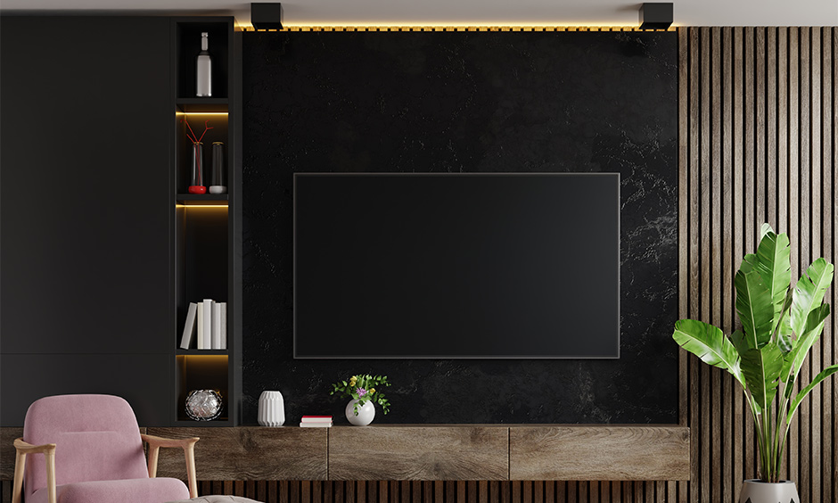 Industrial-style black marble TV unit with rustic wood tones, pink chair, and lush green plants for a chic look.