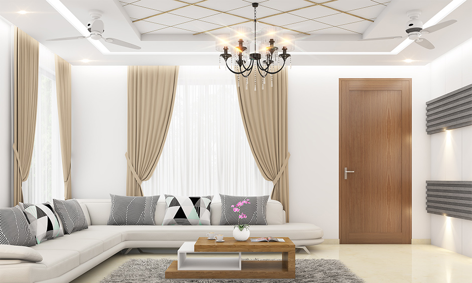 Rectangular living room features a false ceiling with two fans and a central chandelier, blending functionality and elegance