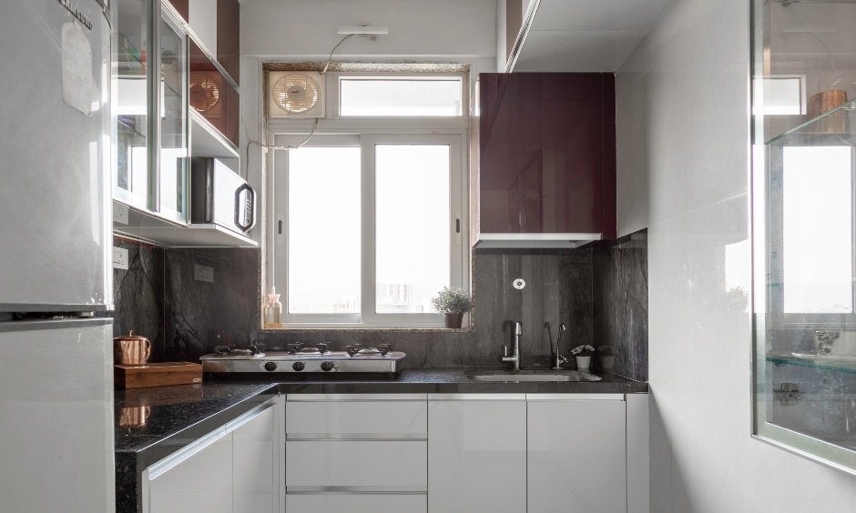 Space-saving L-shaped kitchen in Mumbai 2BHK with white gloss cabinets & modern glass wall units